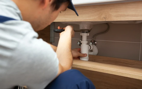 Plombier professionnel intervenant sous un évier de cuisine, travaillant sur l'installation de plomberie