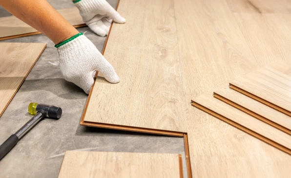 Pose de parquet flottant en intérieur par un ouvrier portant des gants de protection blancs