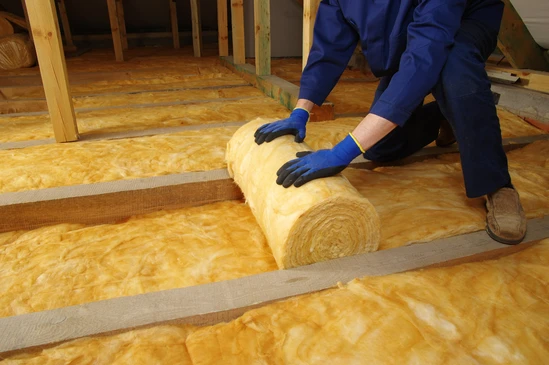 Artisan en tenue de travail et équipement de protection installant de la laine minérale ou de la mousse isolante sur la face intérieure d'un mur existant d'une habitation, avec mise en évidence des panneaux isolants positionnés entre les montants de structure, dans un contexte de rénovation intérieure résidentielle.